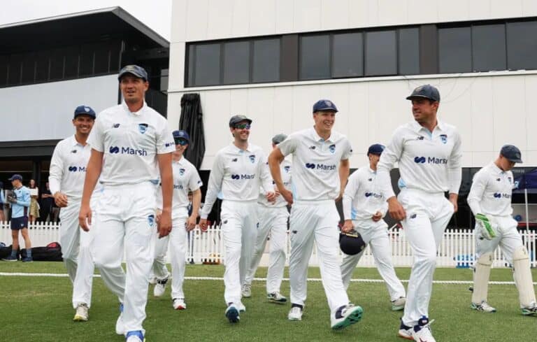 Cricket players walking onto the field in white uniforms during a match.