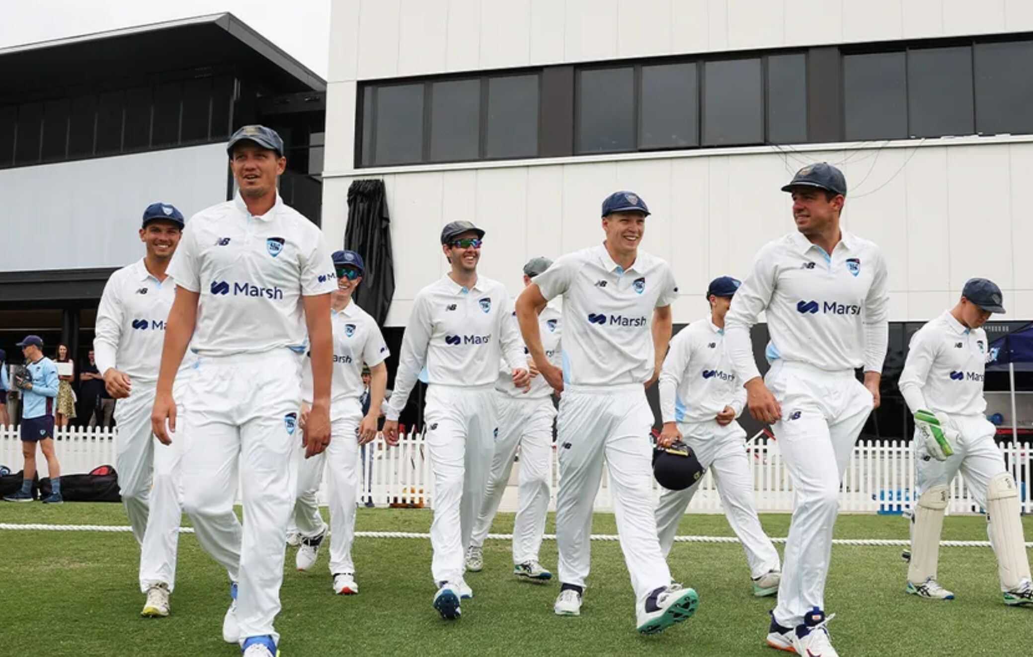 Cricket players walking onto the field in white uniforms during a match.